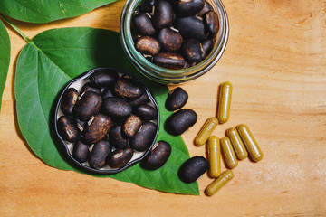 The seeds of Velvet bean or Mucuna pruriens and Pill capsules that contain herbal medicine powder have been used for traditional medicine, selective focused, on wooden background with copy space