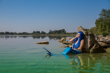 Fototapeta na wymiar Meerjungfrau mit blauer Flosse am Ufer genießt Sonnenbad