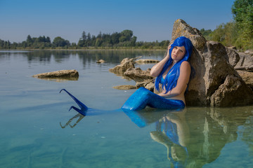 Meerjungfrau mit blauer Flosse am Seeufer