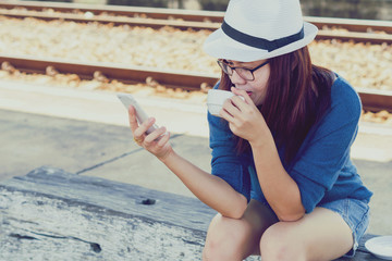Young woman drinking coffee and using a mobile phone on railway station