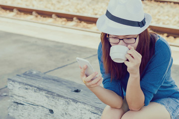Young woman drinking coffee and using a mobile phone on railway station
