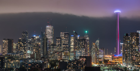 Fototapeta na wymiar Cloud's edge cuts through hot humid night time air in Toronto, Canada. Illuminated skyline as glowing rain cloud quickly moves into downtown core. Hot humid August evening.