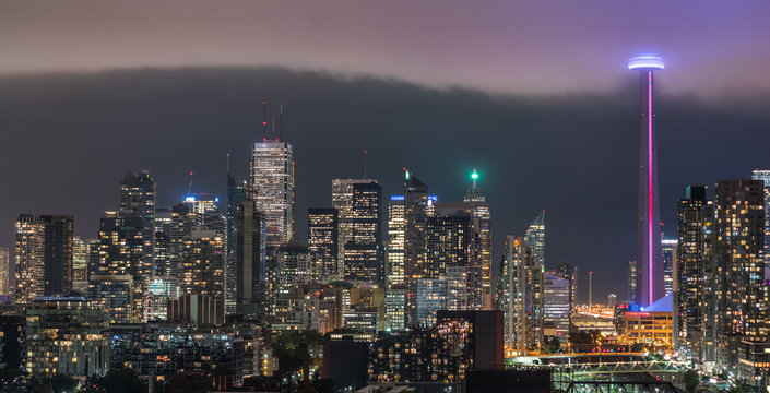 Cloud's edge cuts through hot humid night time air in Toronto, Canada.  Illuminated skyline as glowing rain cloud quickly moves into downtown core.   Hot humid August evening.