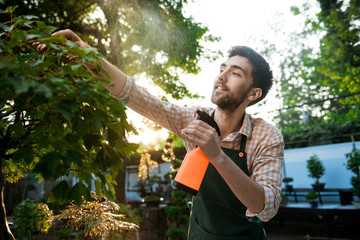 Young handsome cheerful gardener smiling, watering, taking care of plants.