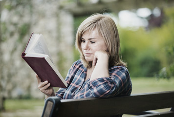 Portrait of  woman sitting on bench and reading book in garden