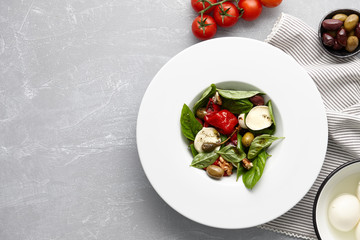 Italian salad with fresh basil leaves, olives, capers, walnuts, mozzarella cheese and red pepper on stone background.