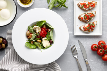 Italian salad with basil leaves, olives, capers, walnuts, mozzarella cheese and red pepper and traditional bruschetta on stone background.