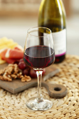 Glass with red wine and tasty snacks on a board on wicker mat