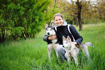 Naklejka na ściany i meble A girl and her dogs husky walking in a park