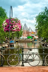 Tuinposter Typical Amsterdam view with bikes, canals and historical buildings. In the back, Nieuwmarkt square is dominated by the gate of the medieval city. © mandritoiu