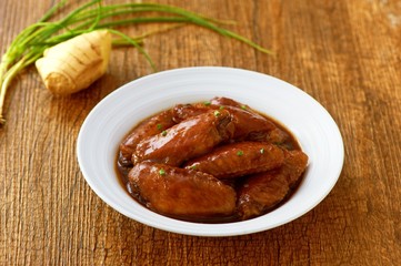 Fried chicken wings on white plate on wooden tray with ginger an