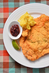 Fried fish fillet on white plate with sauces and lemon