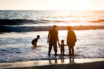 Silhouette family mother, father and young son holding hands, ta
