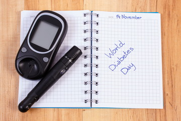 Glucometer with lancet device and world diabetes day written in notebook