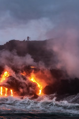 Molten lava from Kalapana lava flowing into Pacific Ocean early morning with silhouette of photographer on cliff