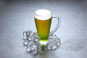Glass of green beer with ice on grey background