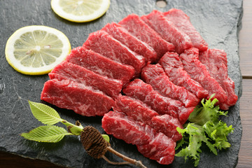 Fresh sliced beef on black rock plate with lemon and herbs