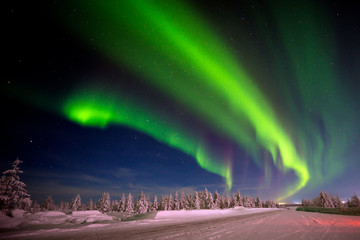 Paysage de nuit d& 39 hiver avec forêt, route et lumière polaire au-dessus des arbres.