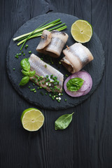 Stone slate with herring fillet over black wooden background