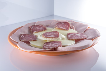 Мясная нарезка с моцареллой на оранжевой тарелке на светлом фоне