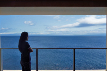 部屋から見える青空と大海原を眺める若い女性