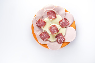 Мясная нарезка с моцареллой на оранжевой тарелке на светлом фоне