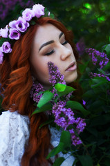 Fototapeta premium Beautiful young redhead girl in lilac garden