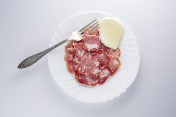Мясная нарезка с моцареллой на оранжевой тарелке на светлом фоне