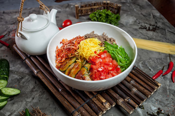 Korean noodle with kimchi, tomatoes, chili in white bowl on bamb