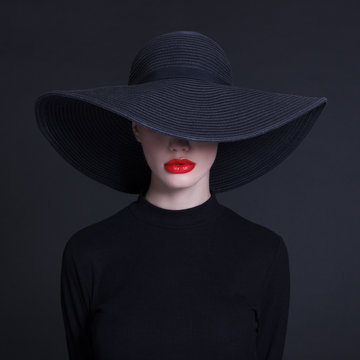Luxury woman in a large black hat and bright lips on black background