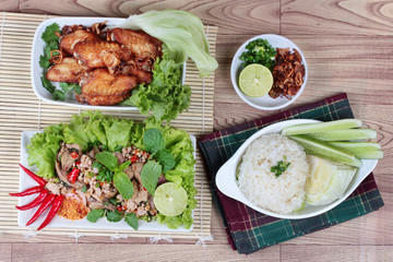 Sticky rice served with fried chicken and  spicy sour mixed herb salad of chicken and liver chicken on wood.   Top view.