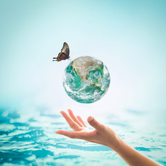 Women's hands holding green planet w/ butterfly drinking potable water from globe on turquoise blue...