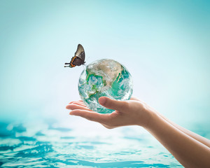 Women's hands holding green planet w/ butterfly drinking potable water from globe on turquoise blue...