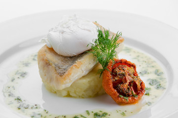 Sudak fried with crushed potatoes and poached egg on white plate