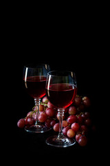 Two glasses of homemade rose wine and grapes on black wooden table. Low key