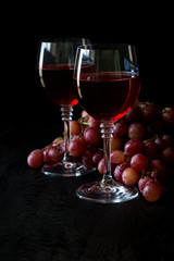 Two glasses of homemade rose wine and grapes on black wooden table. Low key