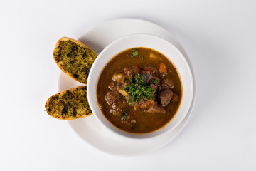 Poucher of Goulash soup with roasted toast and beef on white bac