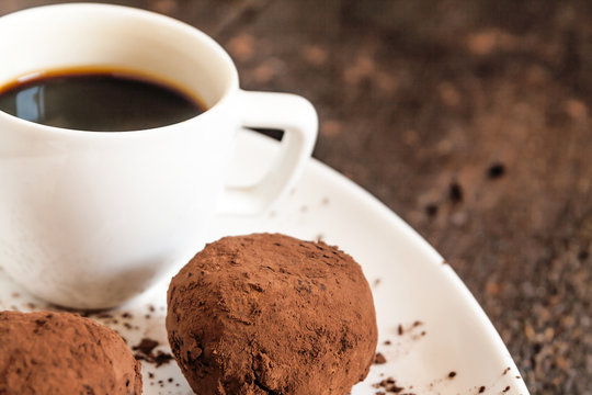 truffles sprinkled with cocoa on plate with  cup of coffee
