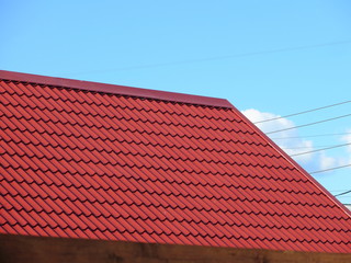 Red modern roof covered with tile effect PVC coated metal roof sheets against a blue sky