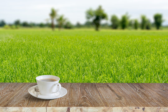 white coffee cup on wood table with green field background, picture for add text