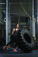 Fototapeta na wymiar Concept: power, strength, healthy lifestyle, sport. Powerful attractive muscular woman CrossFit trainer doing giant tire workout at the gym