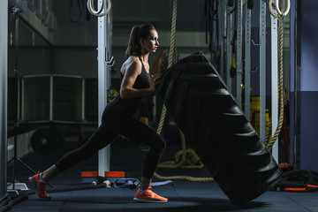 Fototapeta na wymiar Concept: power, strength, healthy lifestyle, sport. Powerful attractive muscular woman CrossFit trainer doing giant tire workout at the gym