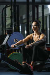 Concept: power, strength, healthy lifestyle, sport. Powerful attractive muscular woman CrossFit trainer do workout on indoor rower at the gym - obrazy, fototapety, plakaty