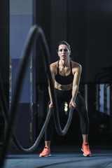 Concept: power, strength, healthy lifestyle, sport. Powerful attractive muscular woman CrossFit trainer do battle workout with ropes at the gym