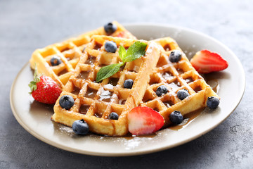 Homemade waffles with berries in plate on grey table