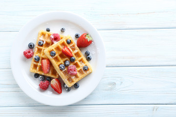 Homemade waffles with berries in plate on blue wooden table