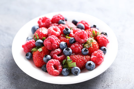 Fresh and sweet berries in white plate on grey background
