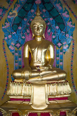 Golden buddha sits in fornt of a decorative floral patterned background in a Buddhist temple in Chiang Mai, Thailand