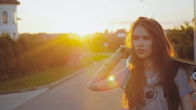 Portrait of a hipster young girl smiling with a skateboard at sunset. Slow motion