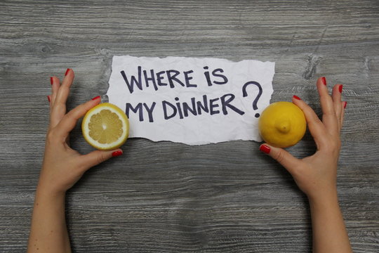 Where is my dinner? Half a lemon in the left hand and whole lemon in the right hand on the gray wooden textural background